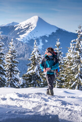 Young backpacker hiking in snowy mountain area with reusable travel mug, against a scenic backdrop of snowy mountains