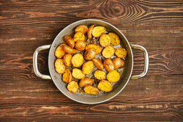 Crispy roasted potatoes in silver skillet on wooden surface