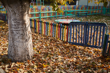 Multicolored fence in a kindergarten made of fallen yellow leaves in autumn