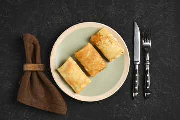 Delicious golden pancakes stuffed with meat served on a rustic plate with cutlery on a dark table