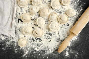 Homemade dumplings with pork meat arranged on a flour-covered kitchen counter with a rolling pin