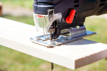 The builder works with a jigsaw. The craftsman cuts the board with a jigsaw.