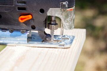 The builder works with a jigsaw. The craftsman cuts the board with a jigsaw.