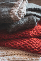 Grey, white and bright orange knitted sweaters in a pile. Stack of cozy handmade clothes. Different knitting patterns concept. Colourful woven jumpers. Knitted comfortable clothing. Knitted fashion.