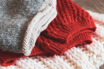 Grey, white and bright orange knitted sweaters in a pile. Stack of cozy handmade clothes. Different knitting patterns concept. Colourful woven jumpers. Knitted comfortable clothing. Knitted fashion.