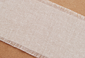 A piece of cotton fabric with fringe on brown cardboard background as a banner