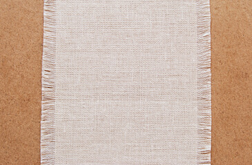 A piece of cotton fabric with fringe on brown cardboard background as a banner