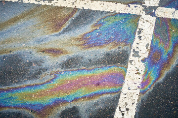 Gasoline or oil spill creating rainbow sheen on asphalt parking lot surface © AleksFil