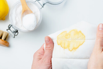 A person holding a stained of fabric near a bowl of baking soda and a lemon, showcasing a DIY cleaning method using natural products to remove stains. top view