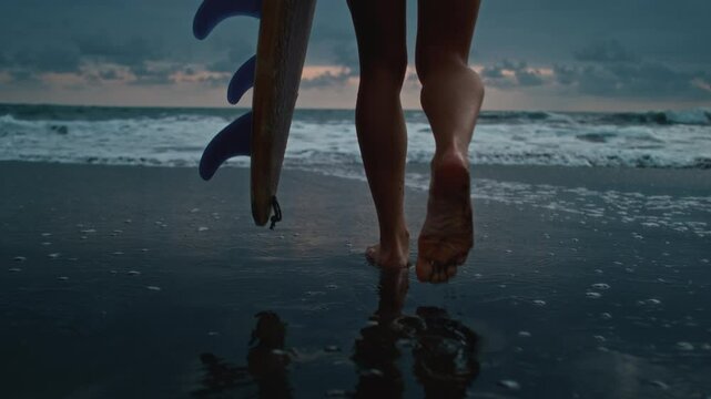 Legs close up, a female surfer with a surfboard, walking along a sandy beach or coast. Feet of a beautiful girl goes surfing in Bali. Surfer female holds a board for the sea, goes into the water, wave - Powered by Adobe