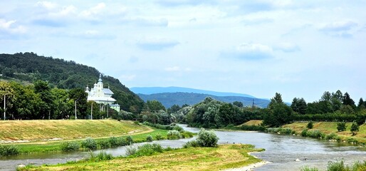 Serene river landscape with distant mountains and a historic building under a cloudy sky