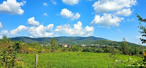 Lush green landscape with rolling hills and a bright blue sky under fluffy clouds in a rural setting