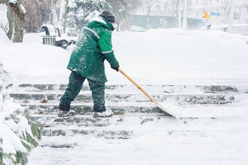Worker shoveling heavy snow off city stair steps during  snowstorm to ensure safety in snowy urban...