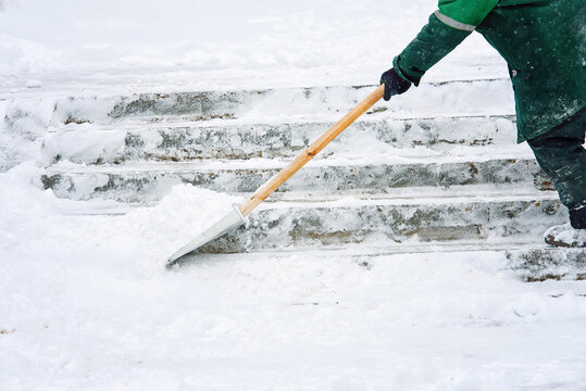 Worker removing snow from slippery stair steps with snow shovel in city during  snowstorm, winter cleanup efforts and safety precautions