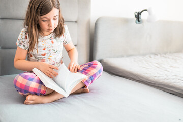 Child reads a book in a bedroom. Little girl reads a bedtime story in her room. Education concept.