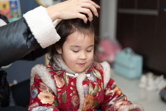 The young Chinese  mother is combing and binding her daughter's hair. Her daughter is wearing traditional Chinese clothes. They're getting ready for celebrating  Chinese New Year.