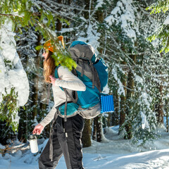 Happy Young Female Backpacker Hiking In The Winter Woods With Hot Tea From Insulated Drink...