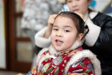 The young Chinese  mother is combing and binding her daughter's hair. Her daughter is wearing...