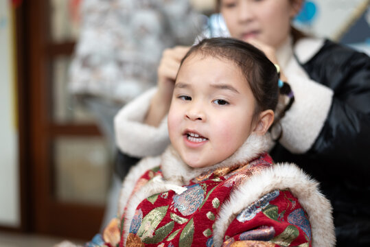 The young Chinese  mother is combing and binding her daughter's hair. Her daughter is wearing traditional Chinese clothes. They're getting ready for celebrating  Chinese New Year.