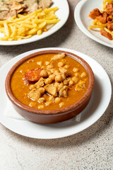Close-up of traditional Spanish chickpea stew with chorizo, pork, and rich broth, served in a rustic clay pot on a white plate