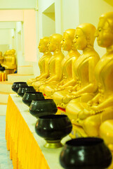 Row of golden Buddha statues with monk's alms bowls in buddhist thai temple, Thailand