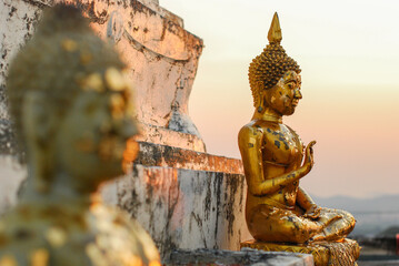 Golden Buddha statue is positioned in a seated posture with gold leaf on surface at sunset