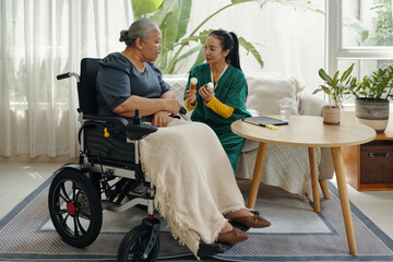 Nurse prescribing medicine to senior woman in wheelchair during her visit to home
