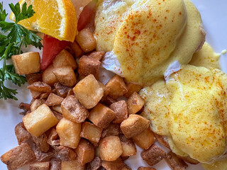 Eggs Benedict And Fried Potatoes With An Orange Garnish