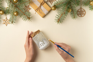 Female hands painting a Christmas candlestick on beige background. Handmade. Flat lay, top view