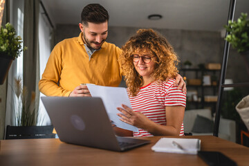 woman work from home on laptop and review document with her boyfriend