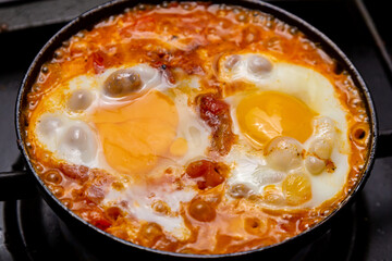 Shakshuka with tomatoes, peppers and onions is fried in a frying pan