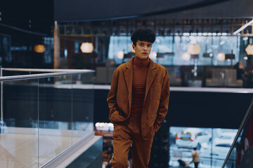 Stylish young man in a brown suit walking in a modern indoor space with large windows and soft lighting