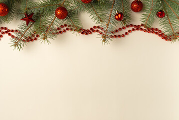 Beige background with Christmas tree branches, red toys and beads. Flat lay, top view. Copy space