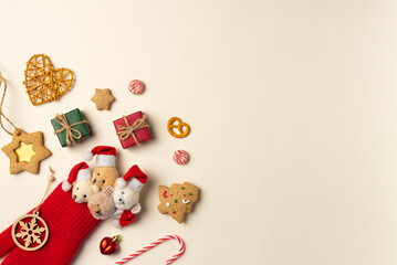 Bears in Christmas caps peek out from mitten with trinkets around on beige background. Flat lay, top view. Copy space