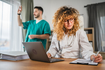 woman doctor in lab coat sit in her medical office and work on laptop