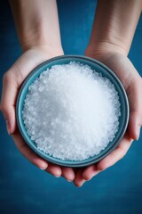 Bowl of coarse salt held between hands against a blue background highlights the natural texture and purity of this essential culinary ingredient