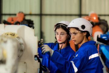 Two Caucasian female engineer, Technician, Machine Operator wearing safety uniform workwear are working, monitor machine operation, check maintenance plan to make a machine work efficiently and safely
