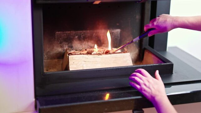 Person igniting firestarter material on wooden log inside modern indoor fireplace with long lighter. Sweden.