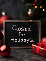 A charming chalkboard sign reading “Closed for Holidays” surrounded by festive decorations, including red ornaments and a gift box. Perfect for conveying seasonal business hours.