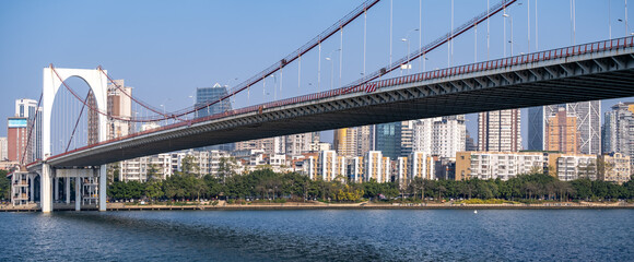 Naklejka premium Panoramic view of the modern Hongguang Bridge with sleek suspension design and iconic white arch spanning the Liujiang River in Liuzhou, Guangxi, China. Urban waterfront skyline in the background.