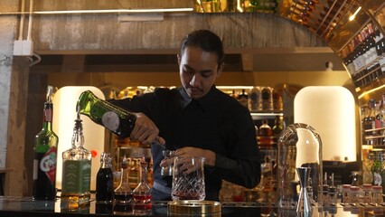 Portrait good looking Asian bartender using jigger measure liquor syrup into mixing glass preparation at luxurious beverage counter bar, neat professional barman costume at nightclub luxury. Vinosity.