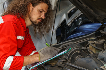 Mechanic inspecting a vehicle engine while taking notes in a workshop