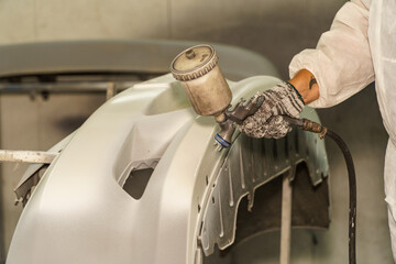 Professional worker applying paint to a vehicle part using a spray gun in a workshop setting during daylight hours