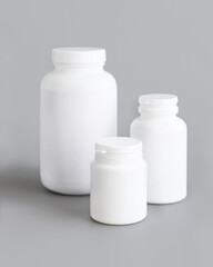 White plastic pill bottles closeup against grey, mockup. Healthcare concept, herbal supplements