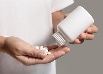 Woman pouring out white pills into hand from white plastic bottle closeup over white shirt