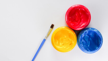 Three jars of red, yellow, and blue paint with a blue-handled brush on a white background. Perfect...