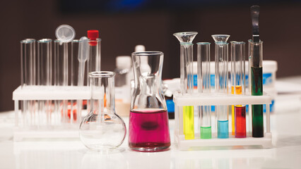A table with many glass beakers and test tubes. One of the beakers is purple. The table is white