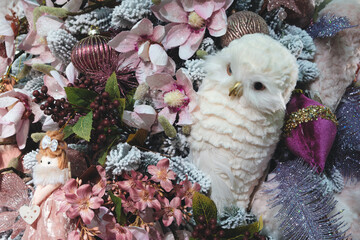 A white owl is sitting on a wreath of flowers. The wreath is decorated with pink flowers and gold ornaments