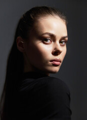 Thoughtful young woman looking over her shoulder with subtle lighting, showcasing a striking expression. Mood and portrait photography concept.