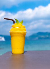 Smoothie made from fresh mango fruits against the backdrop of a seascape. Fruit and yoghurt ice cream decorated with leaves. Glass of tropical dessert close-up.